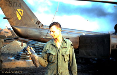 Roger Schmidt holding shrapnel
Jerry Westenskow Photo
Camp Evans the day after the ammunition dump blew up.

This "unknown" was identified as Roger Schmidt (CE) by Guy Sparrow(CE)
Roger was later wounded in a shoot down during August 1968, four klicks west of LZ Barbara with Nick Johnson (AC) and Howard Burbank (P).

