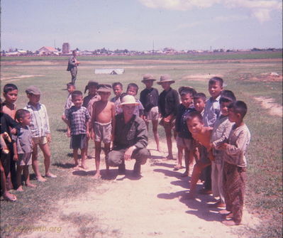 Thien Gao killing time.
Bob Kelly Photo

Thien Gao. Killing time on medcap mission. Bob Kelly in NVA ? headgear, boy in my hat.
